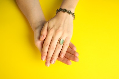 Beautiful bijouterie. Woman wearing stylish ring and bracelet on yellow background, top view