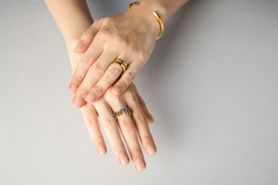 Beautiful bijouterie. Woman wearing stylish rings and bracelet on light grey background, closeup