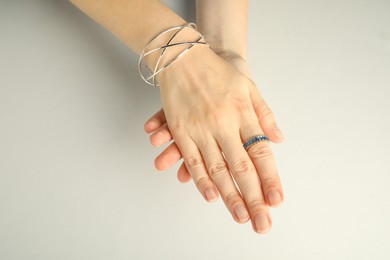 Beautiful bijouterie. Woman wearing stylish ring and bracelet on light grey background, top view