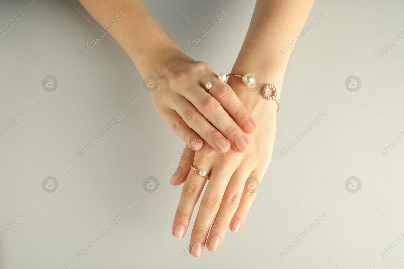 Photo of Beautiful bijouterie. Woman wearing stylish rings and bracelet on light grey background, top view