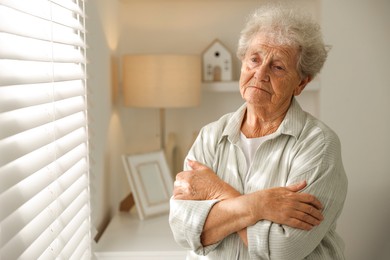 Photo of Loneliness concept. Sad senior woman near window at home