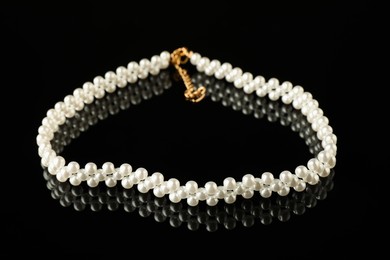 Photo of Beautiful bijouterie. Elegant bracelet on black mirror surface, closeup