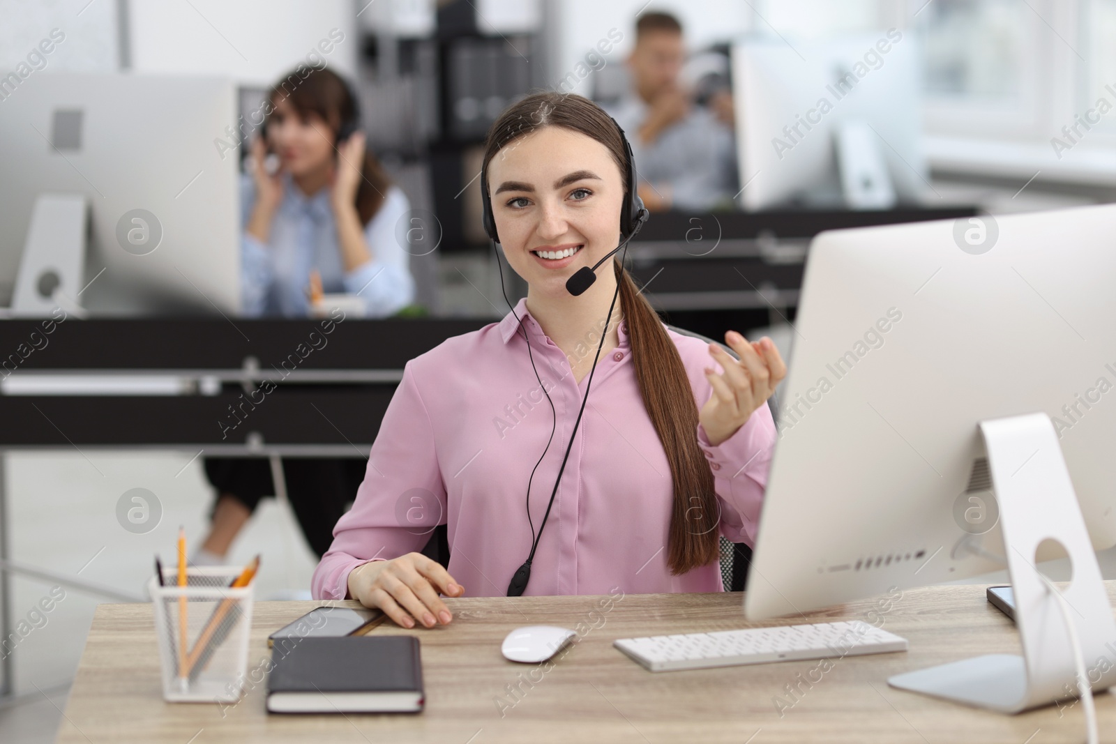 Photo of Saleswoman talking to client via headset at desk in office