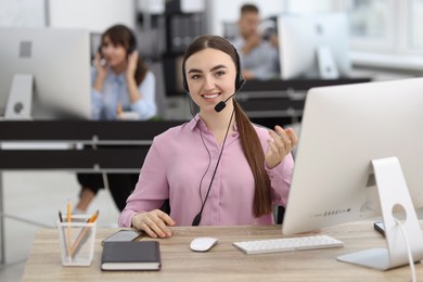 Photo of Saleswoman talking to client via headset at desk in office