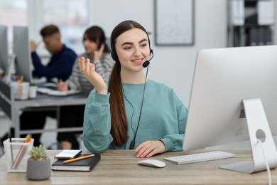 Photo of Saleswoman talking to client via headset at desk in office