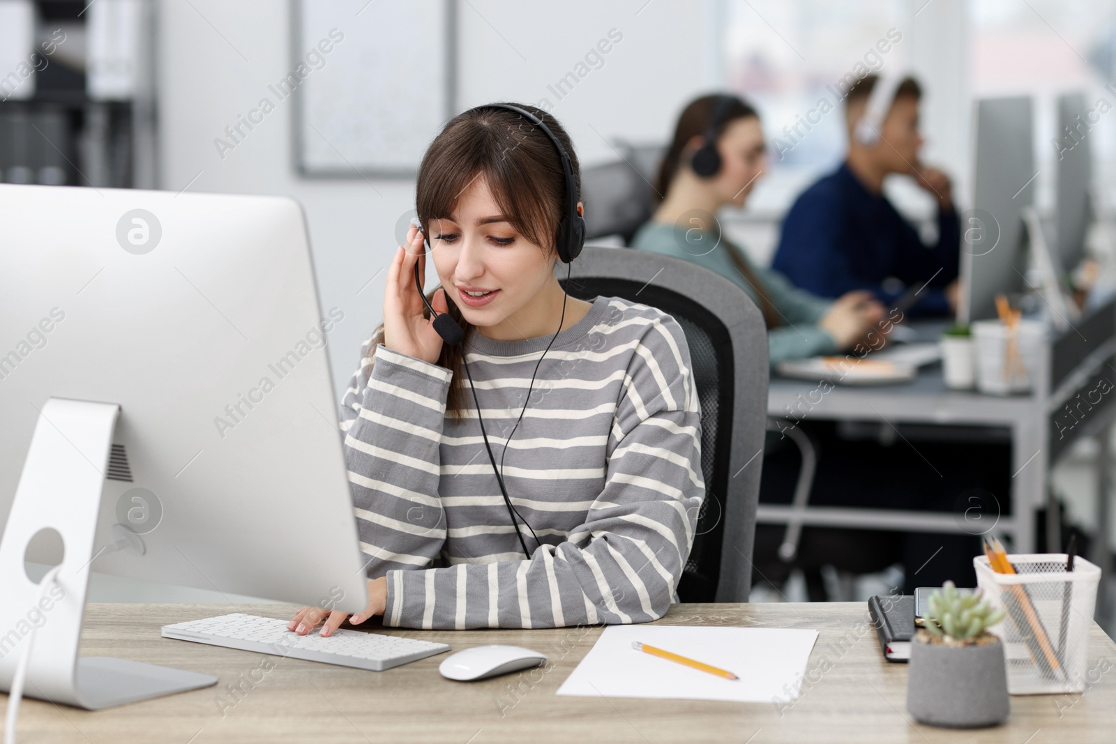 Photo of Saleswoman talking to client via headset at desk in office