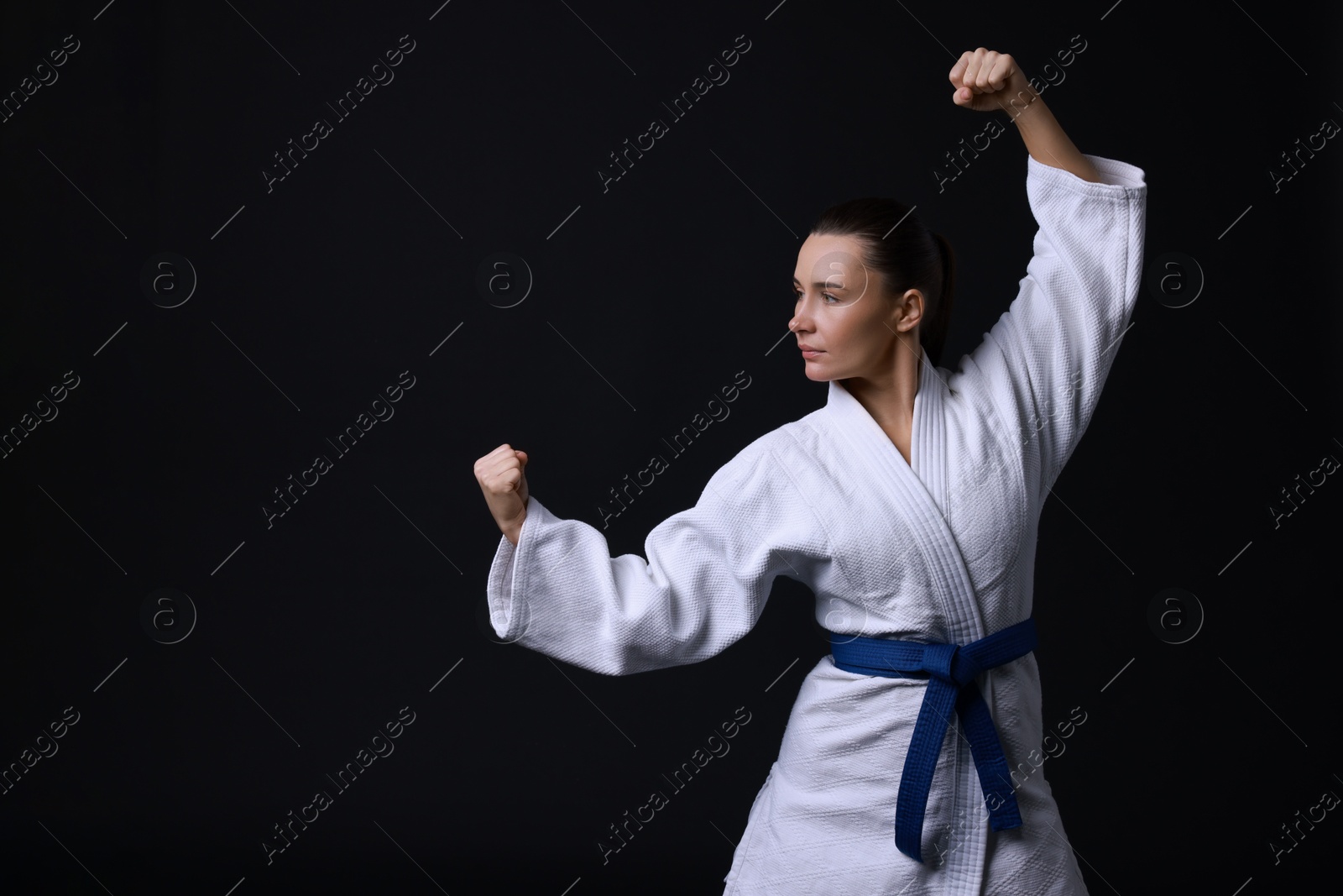 Photo of Young woman in kimono practicing karate on black background, space for text