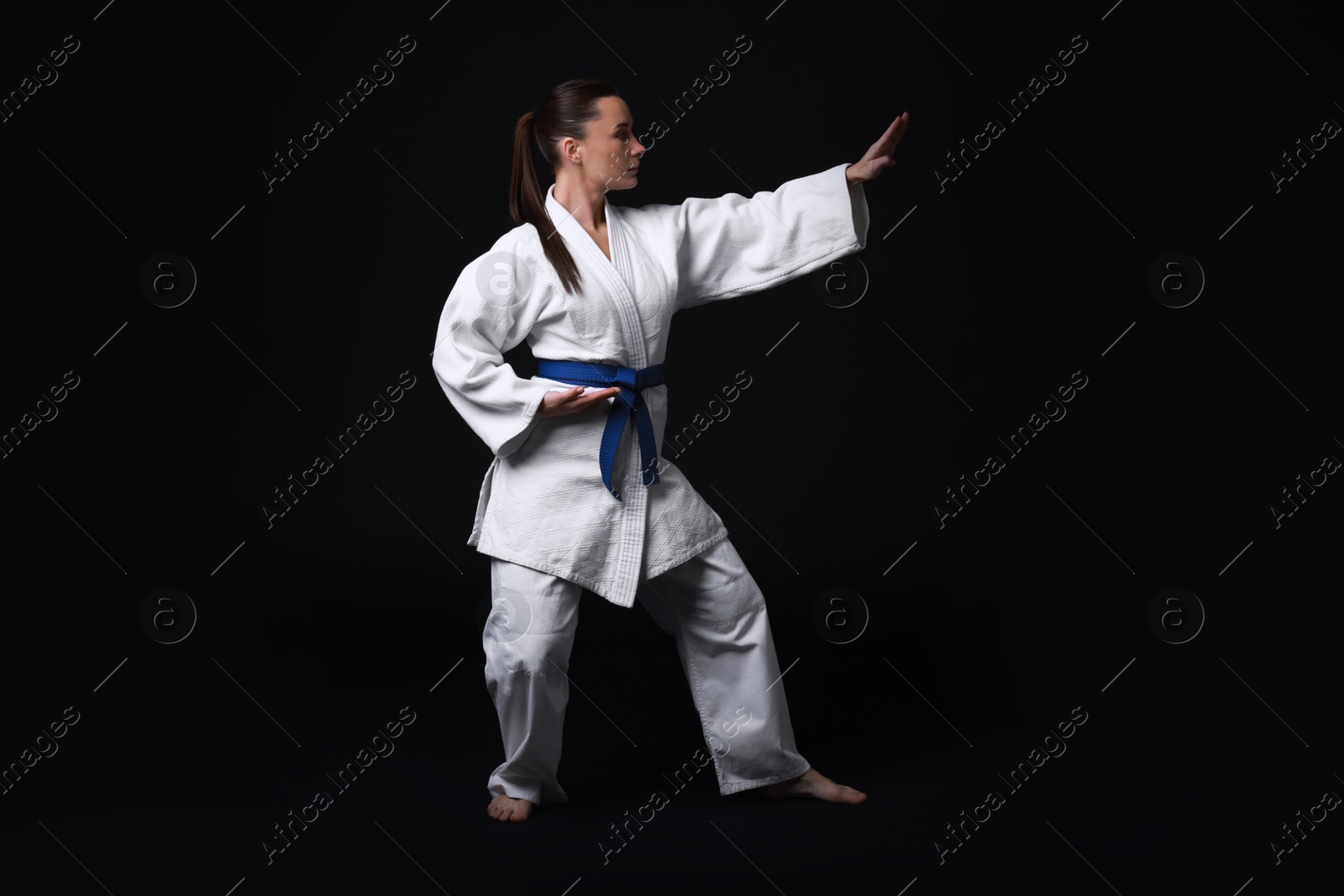 Photo of Young woman in kimono practicing karate on black background