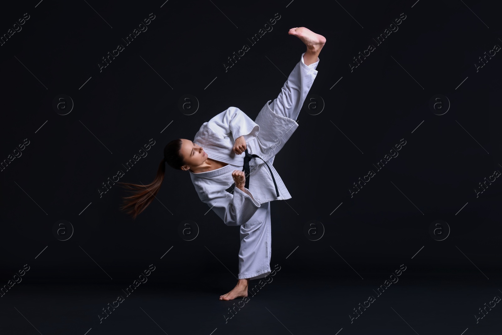 Photo of Young woman in kimono practicing karate on black background