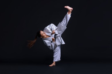 Photo of Young woman in kimono practicing karate on black background