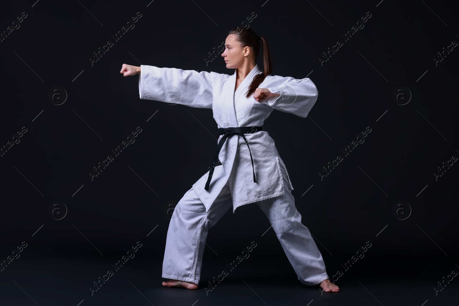 Photo of Young woman in kimono practicing karate on black background