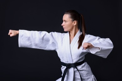 Photo of Young woman in kimono practicing karate on black background