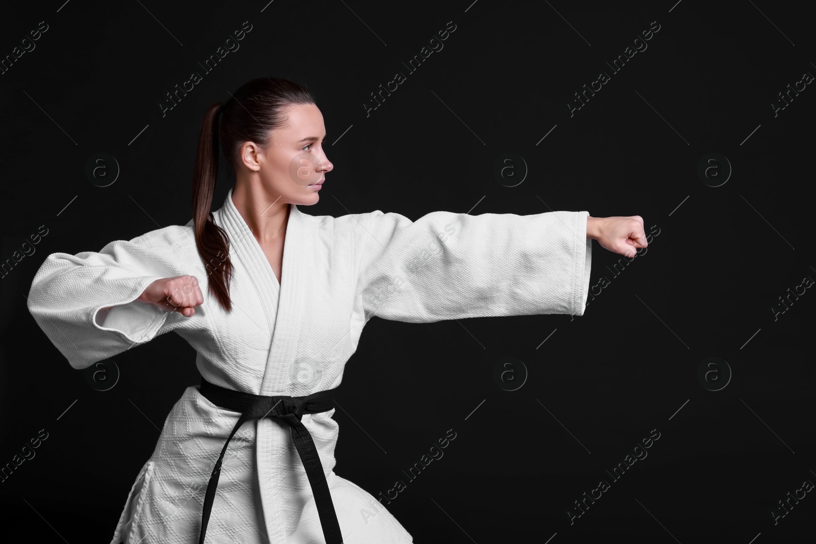 Photo of Young woman in kimono practicing karate on black background