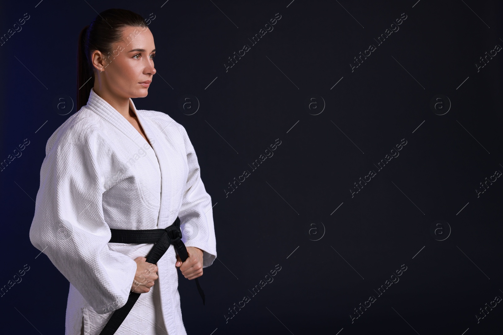 Photo of Karate fighter in kimono on dark background, space for text