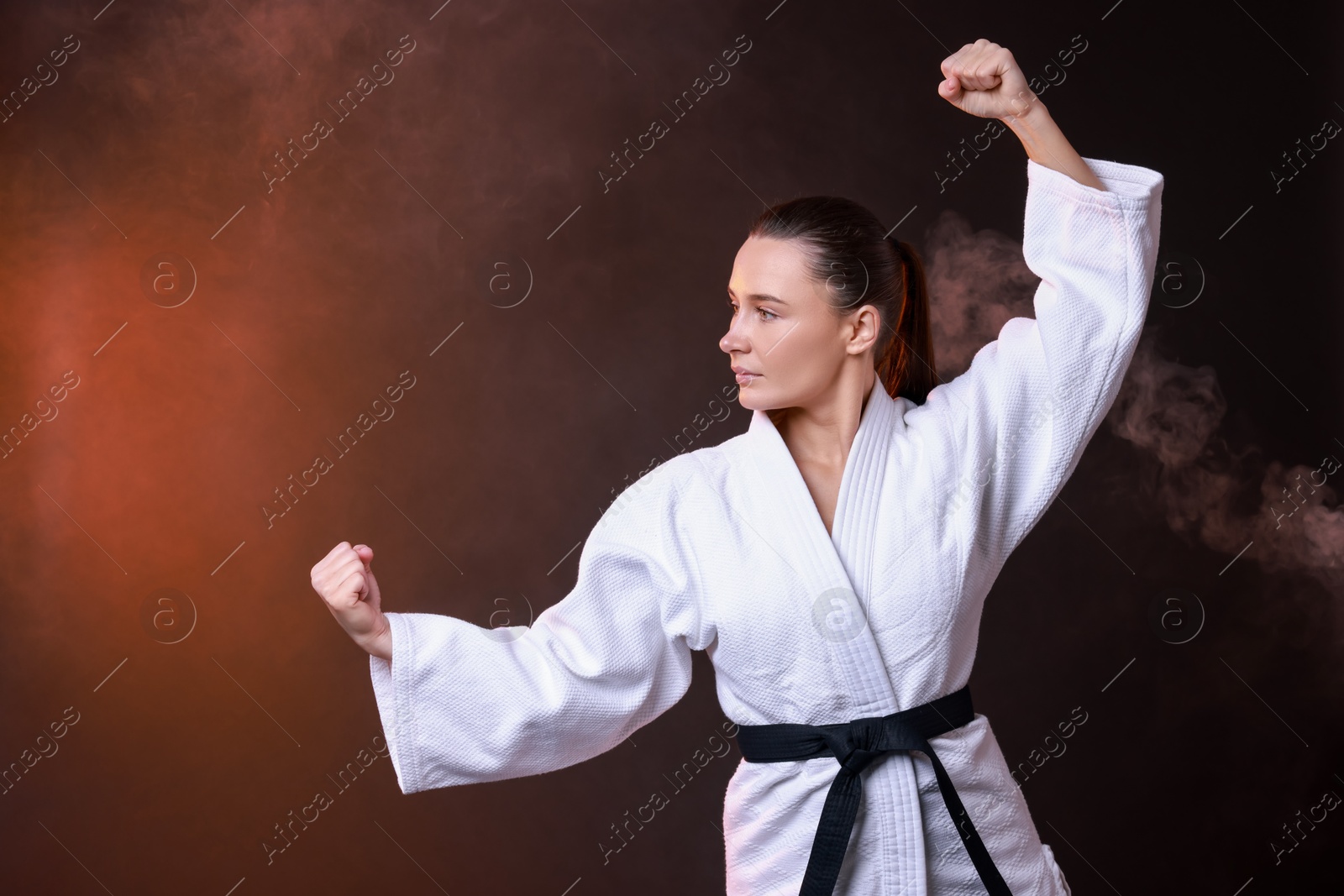 Photo of Young woman in kimono practicing karate on dark background, space for text