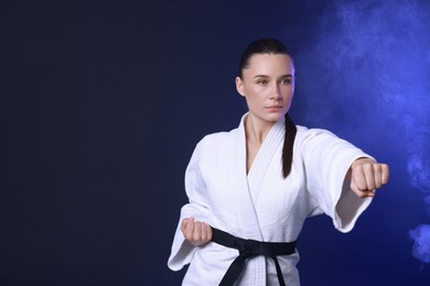 Photo of Karate fighter in kimono on dark blue background, space for text