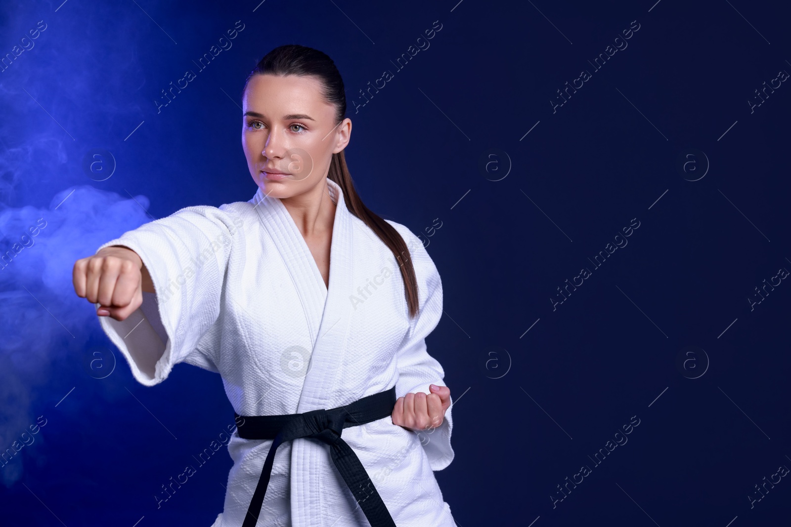 Photo of Karate fighter in kimono on dark blue background, space for text