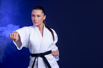 Photo of Karate fighter in kimono on dark blue background, space for text