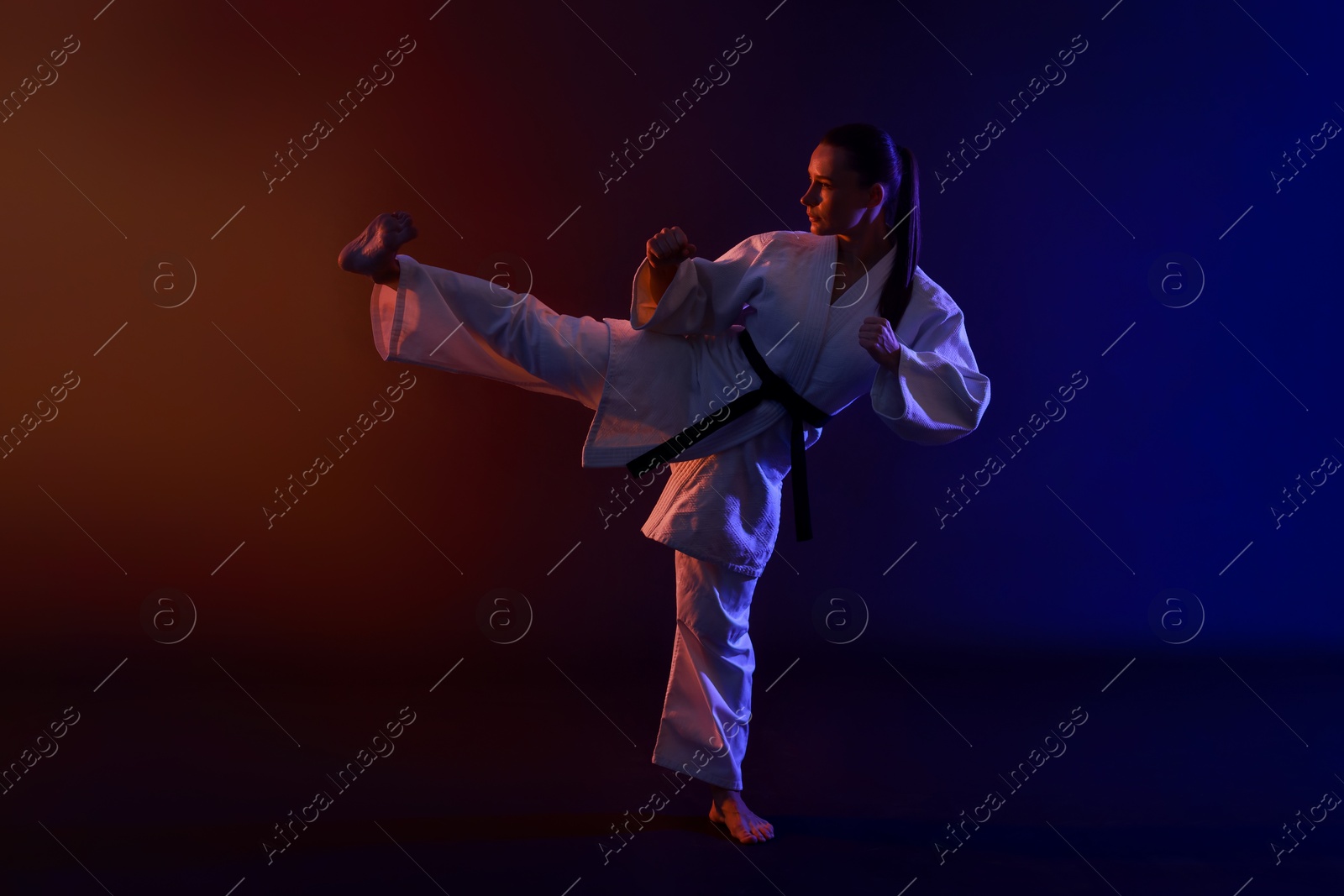 Photo of Young woman in kimono practicing karate on dark background