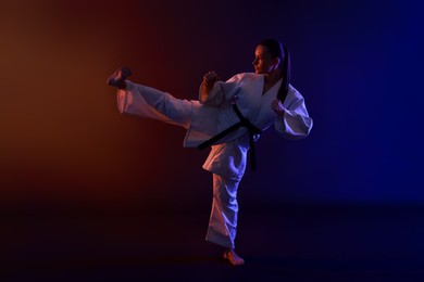 Photo of Young woman in kimono practicing karate on dark background