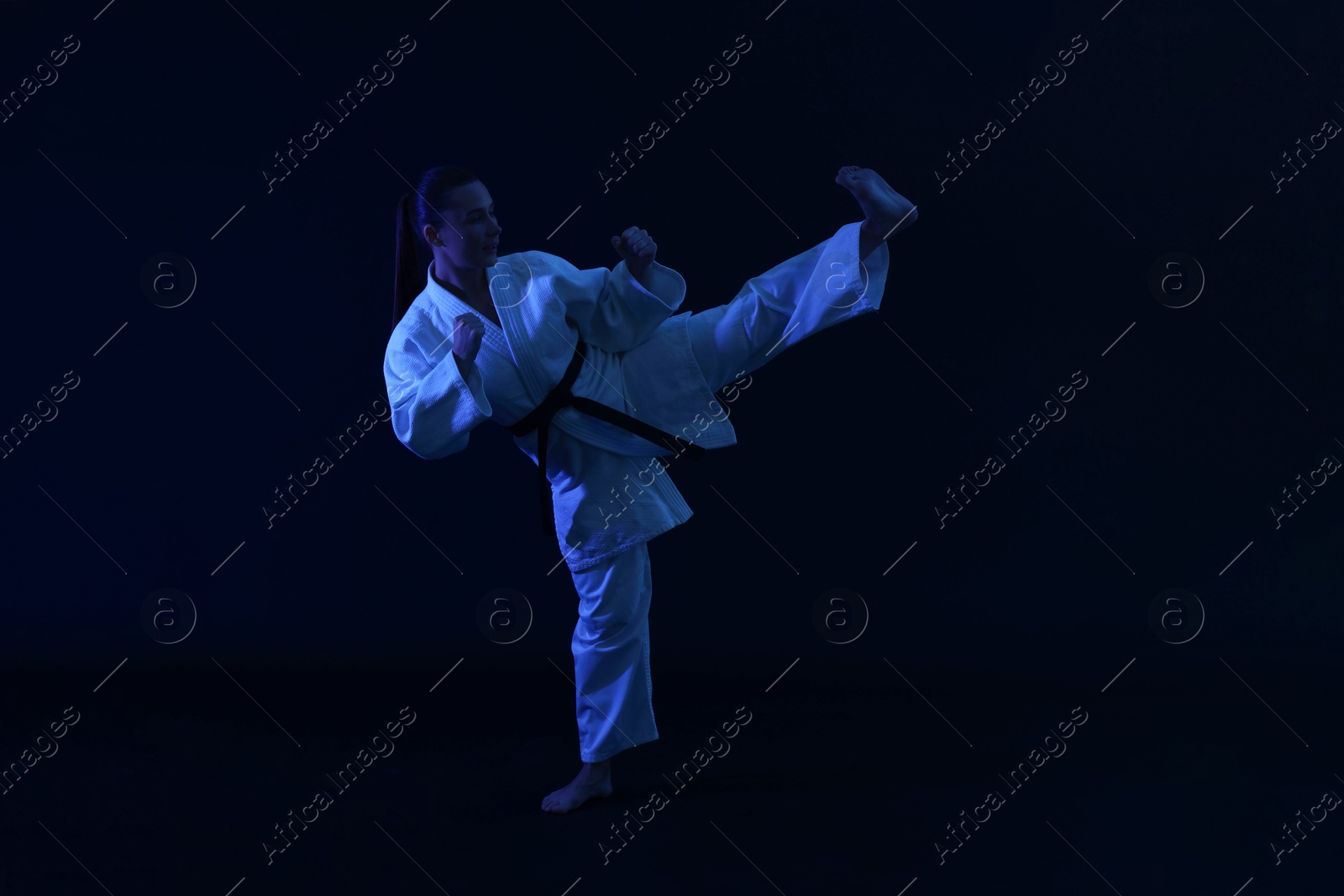 Photo of Young woman in kimono practicing karate on dark background