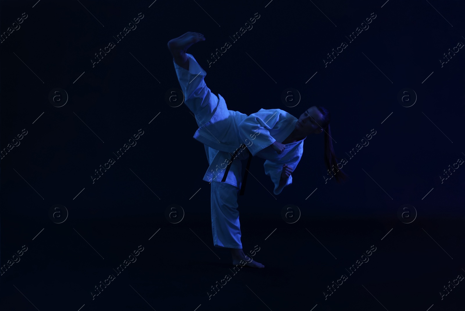 Photo of Young woman in kimono practicing karate on dark background