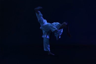 Photo of Young woman in kimono practicing karate on dark background