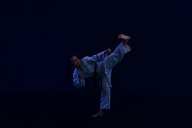 Photo of Young woman in kimono practicing karate on dark background