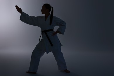 Photo of Silhouette of woman in kimono practicing karate on light background, space for text