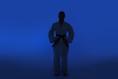 Photo of Silhouette of karate fighter in kimono on dark blue background