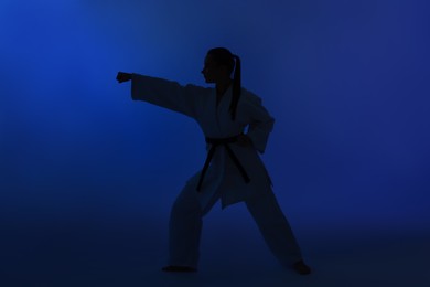 Photo of Silhouette of woman in kimono practicing karate on dark blue background