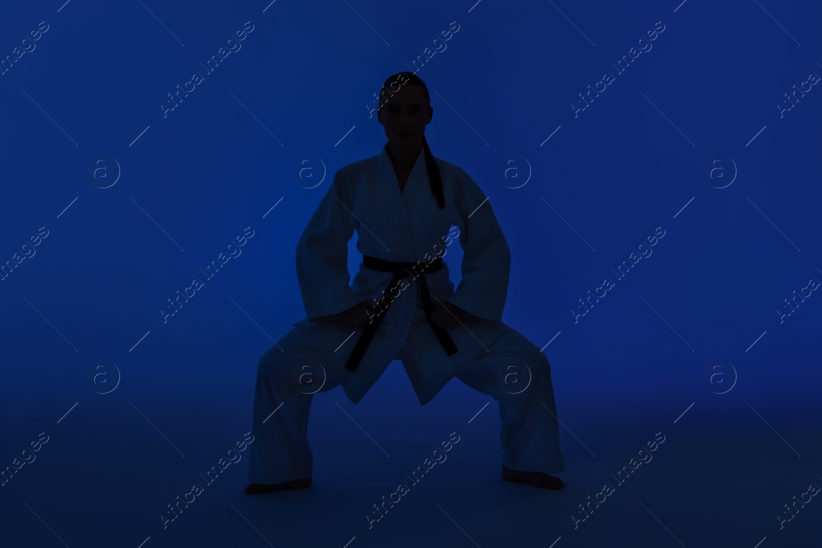 Photo of Silhouette of woman in kimono practicing karate on dark blue background