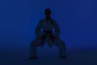 Photo of Silhouette of woman in kimono practicing karate on dark blue background