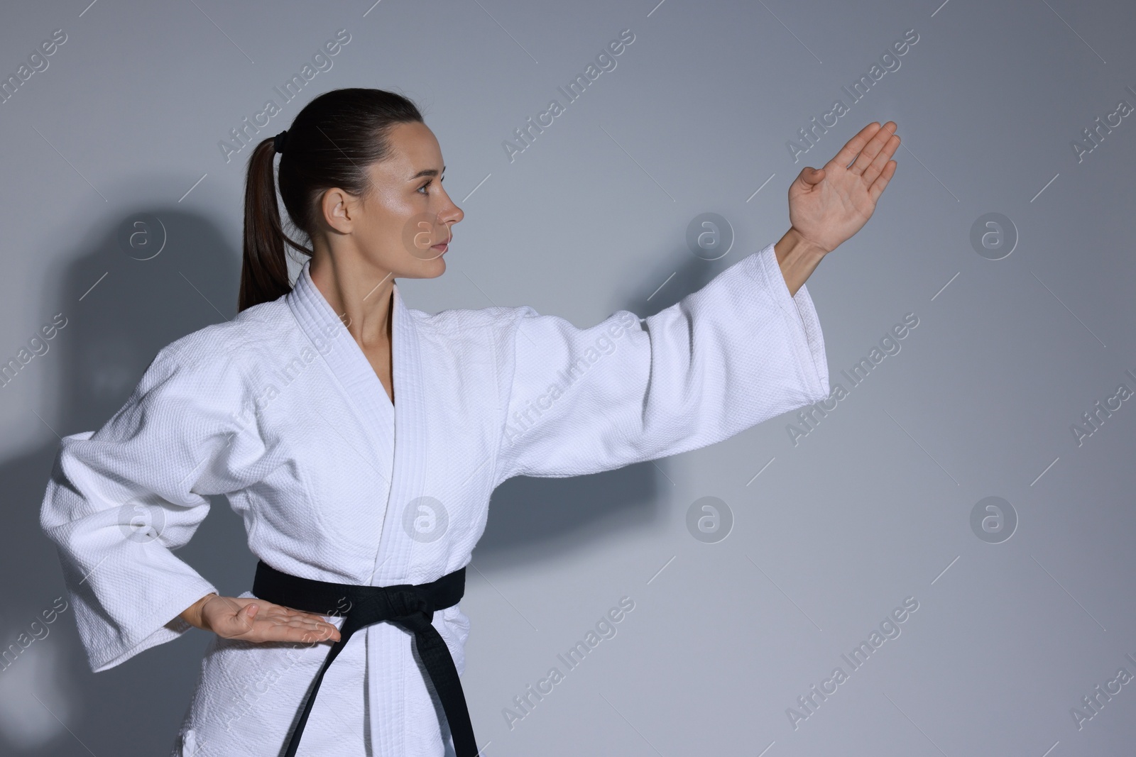 Photo of Young woman in kimono practicing karate on grey background