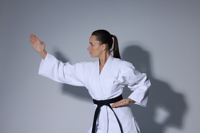 Photo of Young woman in kimono practicing karate on grey background