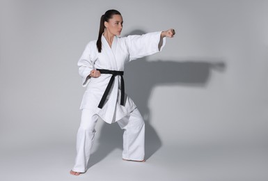 Photo of Young woman in kimono practicing karate on grey background, space for text