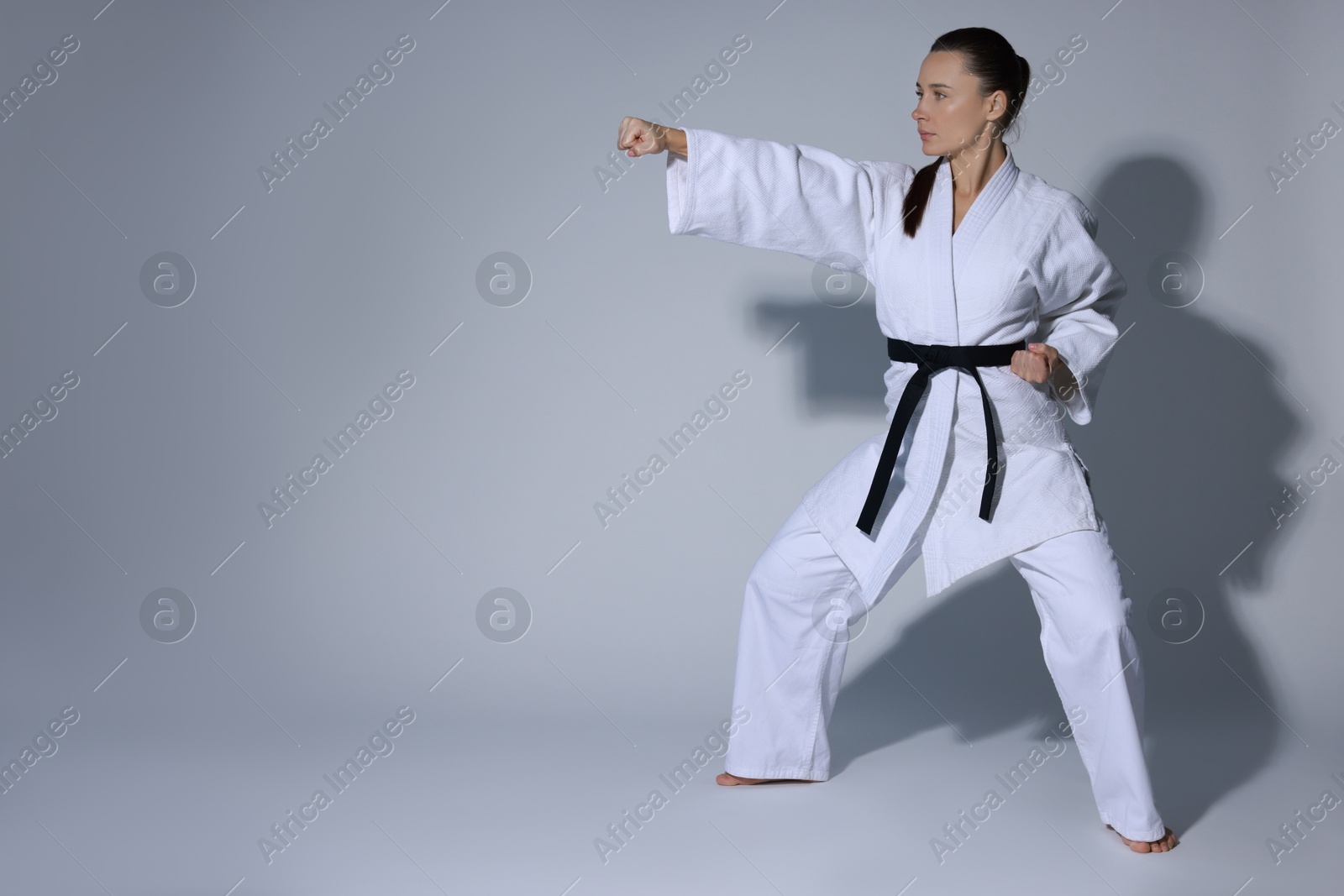 Photo of Young woman in kimono practicing karate on grey background, space for text