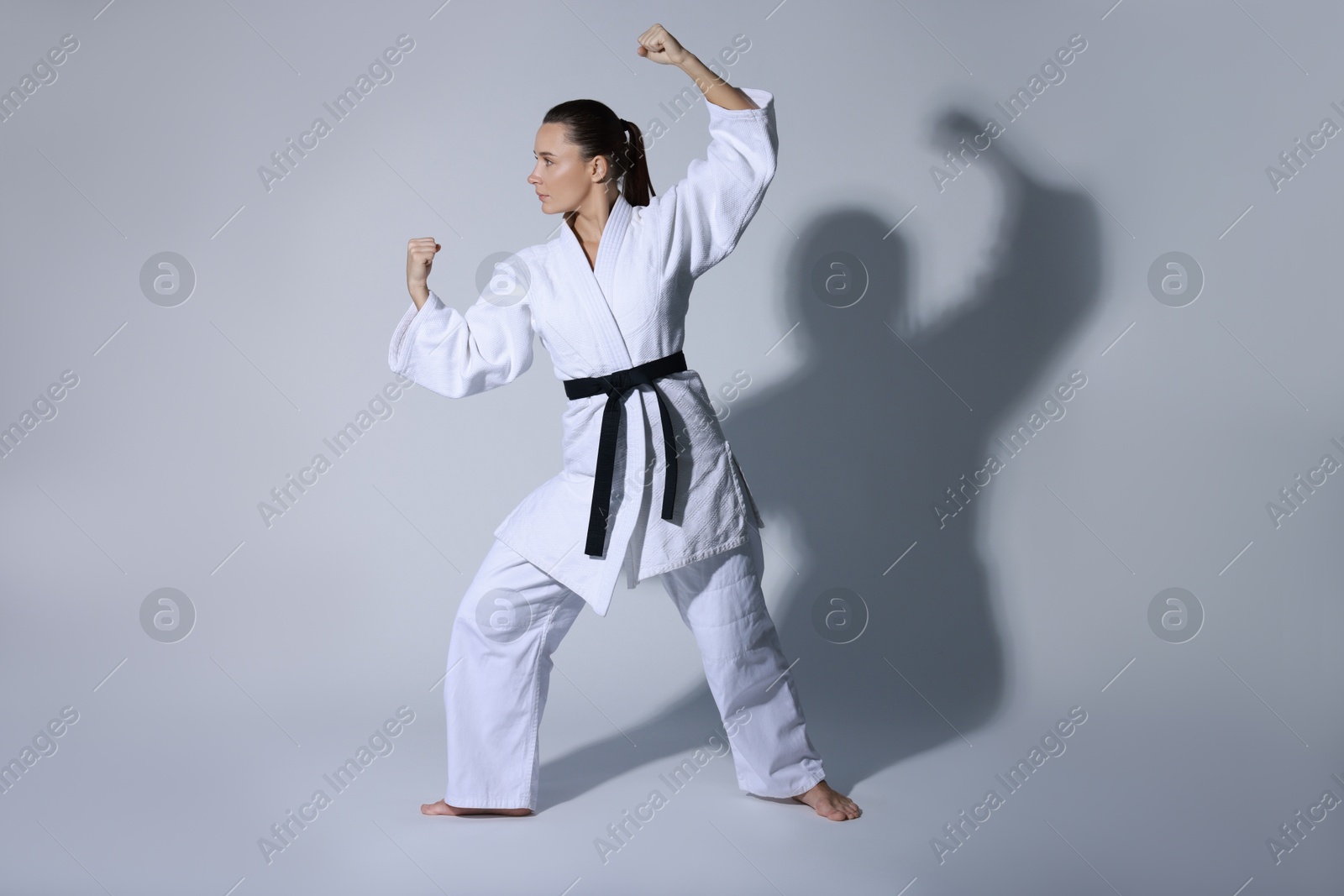 Photo of Young woman in kimono practicing karate on grey background, space for text