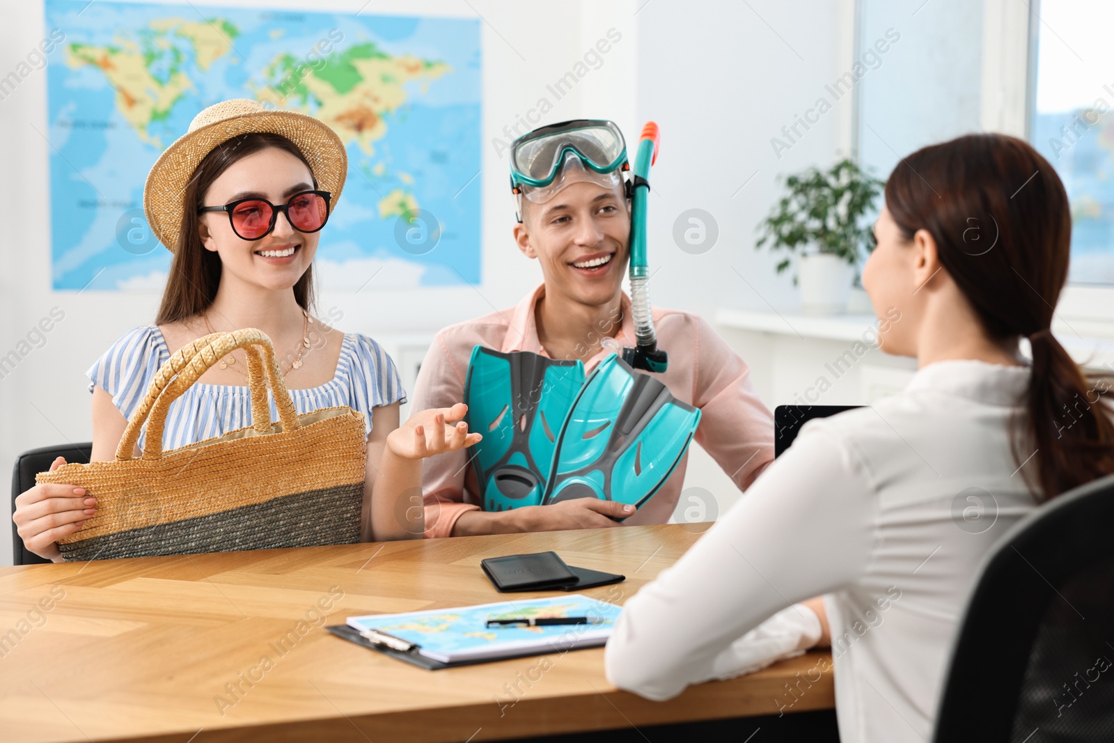 Photo of Happy couple planning vacation with travel agent at wooden table in office