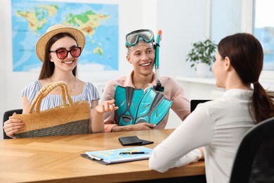 Photo of Happy couple planning vacation with travel agent at wooden table in office