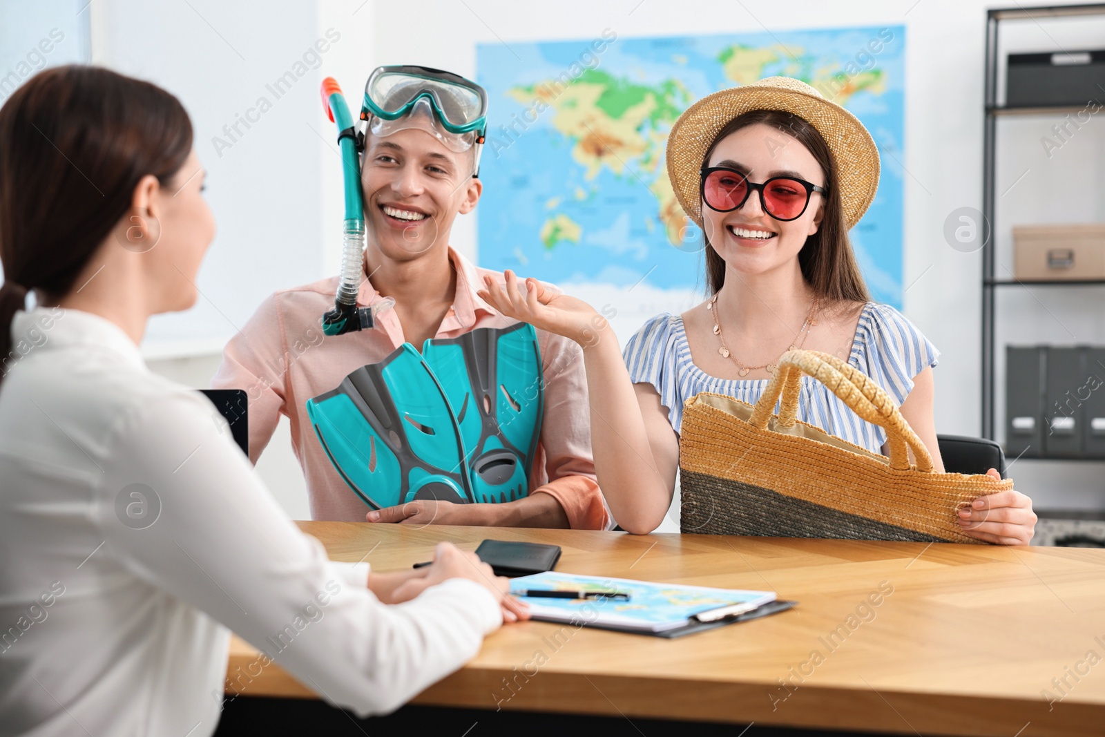 Photo of Happy couple planning vacation with travel agent at wooden table in office