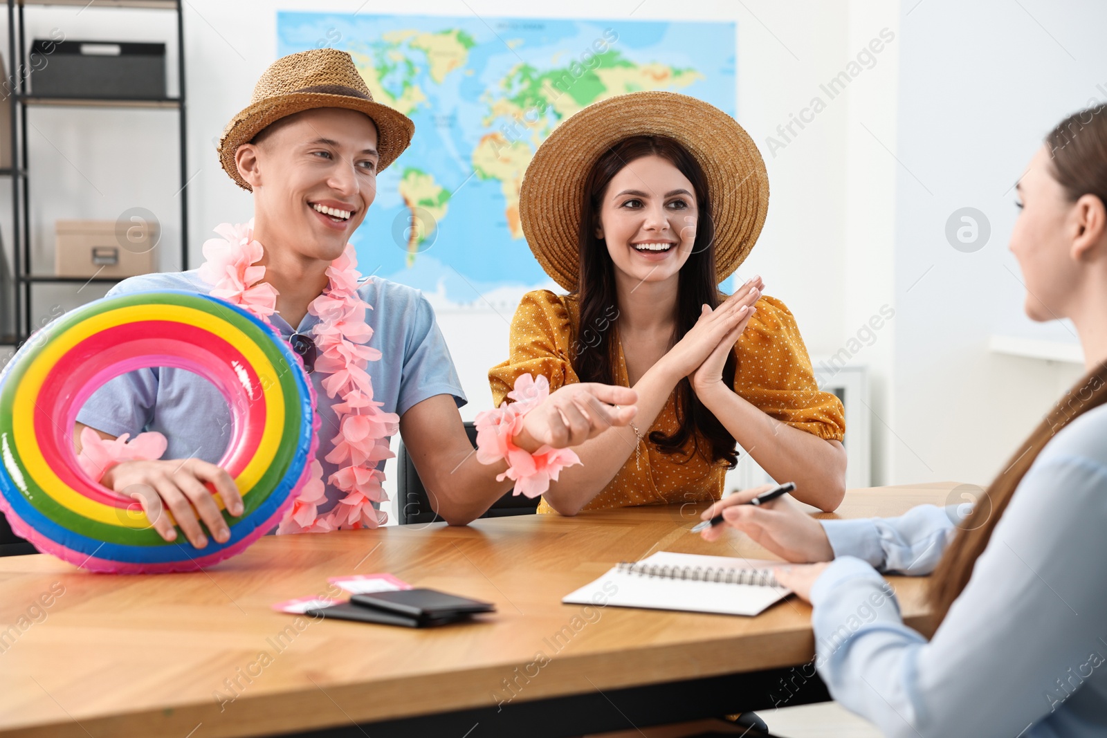 Photo of Happy couple planning vacation with travel agent at wooden table in office