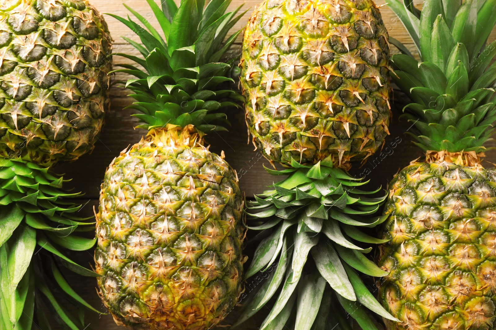 Photo of Fresh ripe pineapples on wooden table, above view