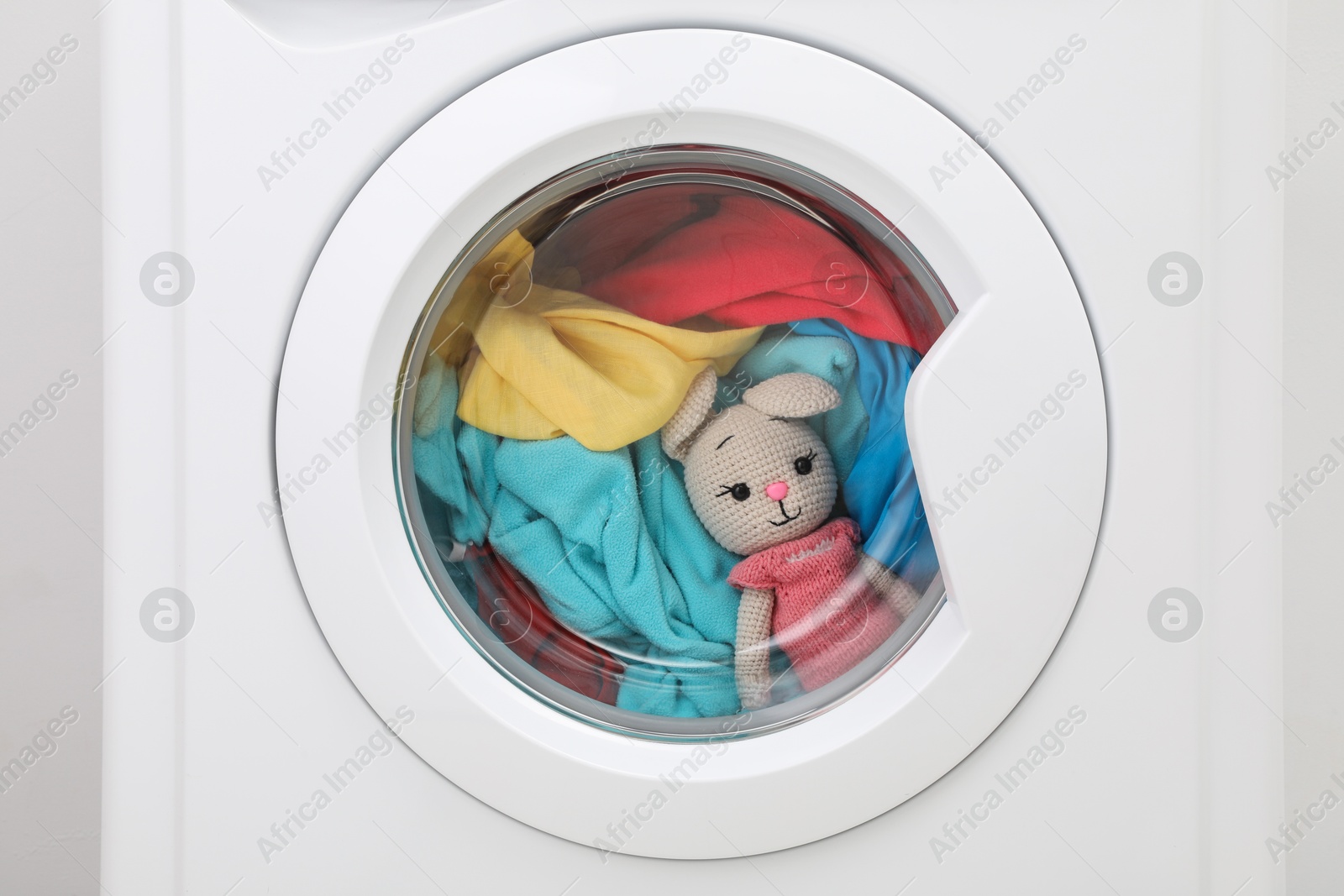 Photo of Washing machine with clothes and toy bunny as background, closeup