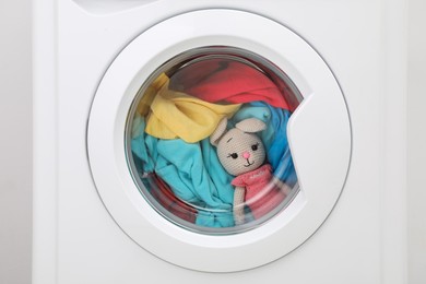 Photo of Washing machine with clothes and toy bunny as background, closeup