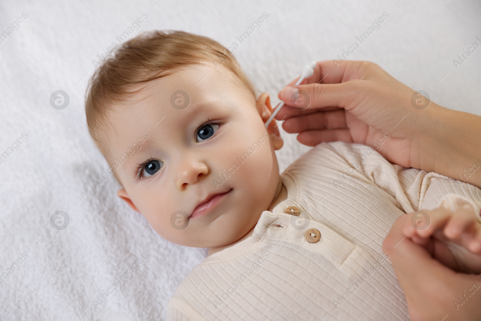 Photo of Mother cleaning ear of her cute little baby with cotton swab on bed, closeup