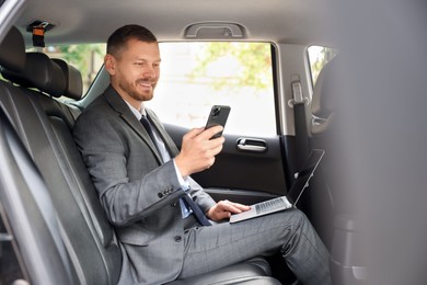 Photo of Man with laptop and smartphone in modern car