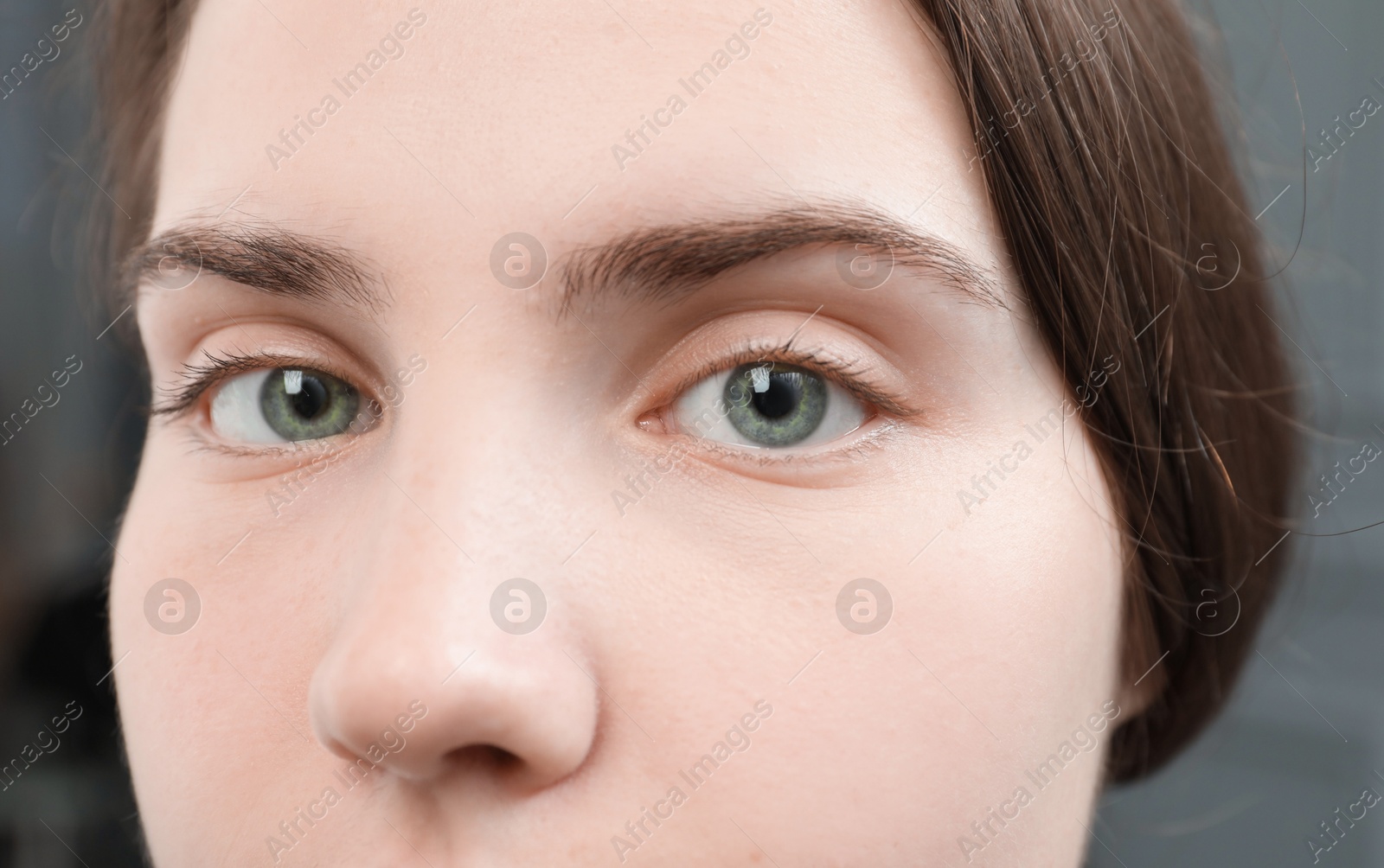 Photo of Closeup view of young woman with beautiful blue eyes on grey background