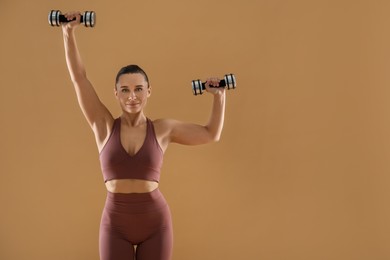 Photo of Woman exercising with dumbbells on beige background, space for text