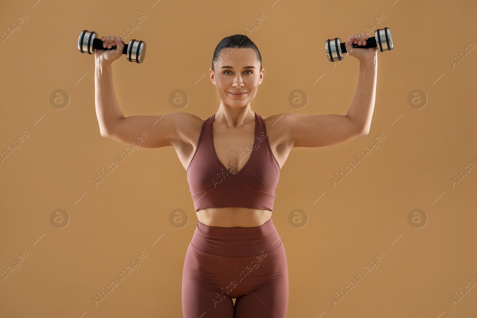 Photo of Woman exercising with dumbbells on beige background